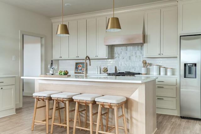 kitchen with an island with sink, sink, light wood-type flooring, and stainless steel fridge with ice dispenser