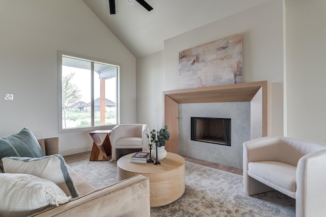 living room featuring a tile fireplace, vaulted ceiling, ceiling fan, and light hardwood / wood-style floors