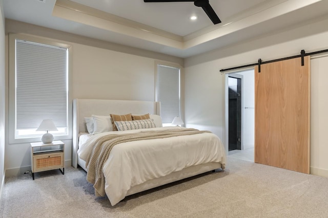 carpeted bedroom with a tray ceiling, a barn door, and ceiling fan