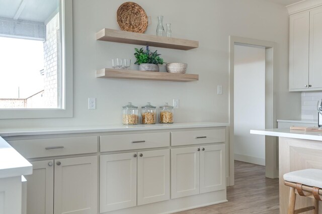 bar with a healthy amount of sunlight, light hardwood / wood-style floors, decorative backsplash, and white cabinets