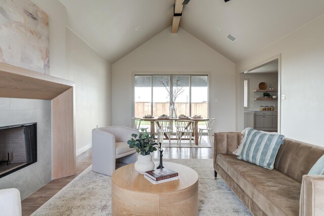 living room with lofted ceiling with beams, a tile fireplace, and light wood-type flooring