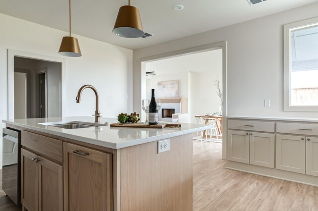 kitchen featuring decorative light fixtures, light hardwood / wood-style floors, sink, and a center island with sink