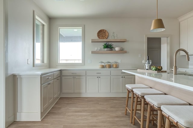 kitchen with pendant lighting, sink, white cabinets, a kitchen bar, and light wood-type flooring