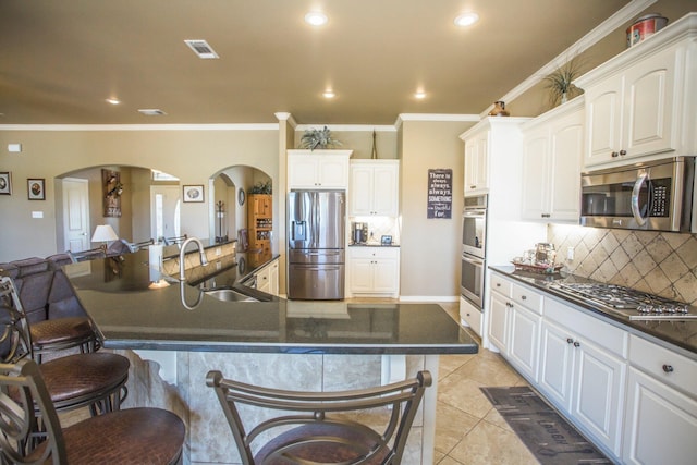 kitchen with arched walkways, a sink, dark countertops, a kitchen breakfast bar, and stainless steel appliances
