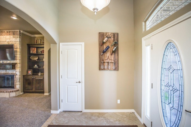 foyer featuring arched walkways, light tile patterned floors, a towering ceiling, and a brick fireplace