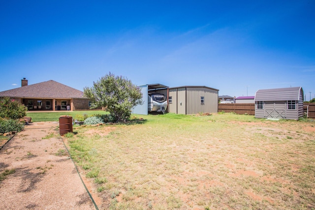 view of yard featuring a carport, a storage shed, an outdoor structure, and fence
