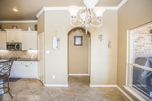 kitchen featuring tasteful backsplash, arched walkways, white cabinetry, a chandelier, and stainless steel microwave