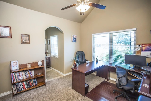 carpeted home office featuring high vaulted ceiling, arched walkways, baseboards, and ceiling fan