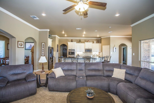 living room featuring ornamental molding, visible vents, a ceiling fan, and arched walkways