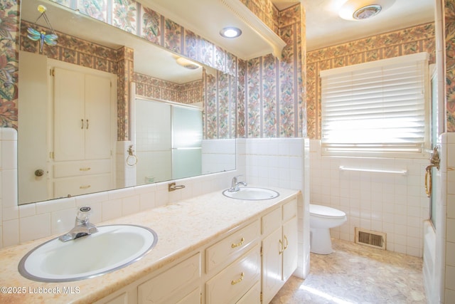 3404 59th St, Lubbock, TX 79413 - full bath with wallpapered walls, toilet, double vanity, tile walls, and a wainscoted wall