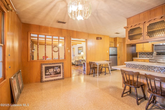 3404 59th St, Lubbock, TX 79413 - kitchen with appliances with stainless steel finishes, light flooring, wood walls, decorative backsplash, and a chandelier