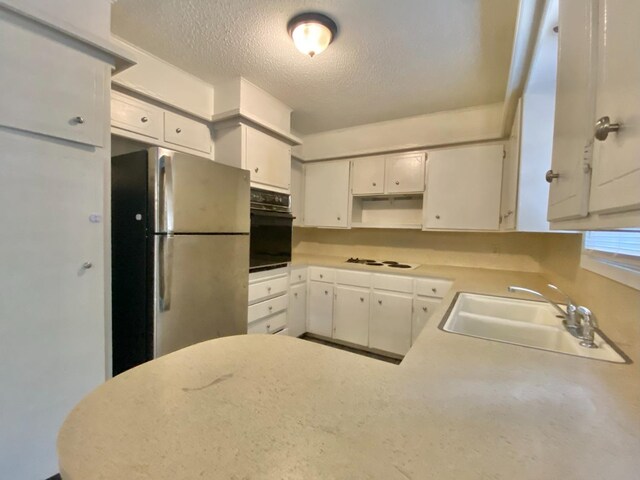 kitchen featuring black oven, stainless steel refrigerator, white cabinetry, and sink