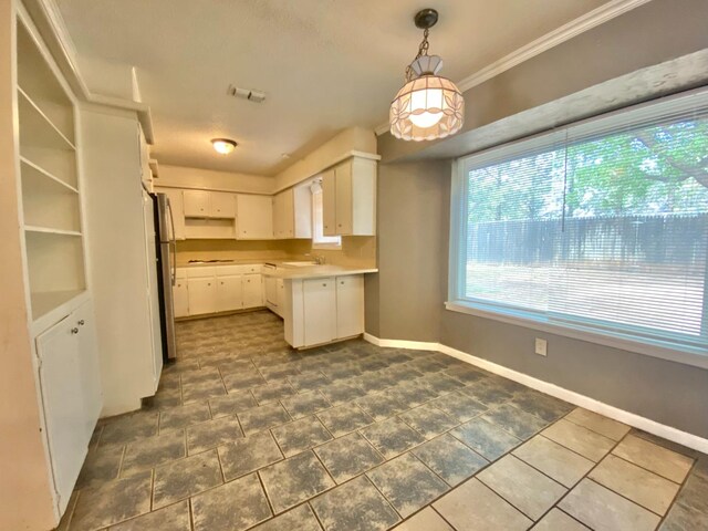 kitchen with stainless steel refrigerator, sink, ornamental molding, decorative light fixtures, and white cabinets