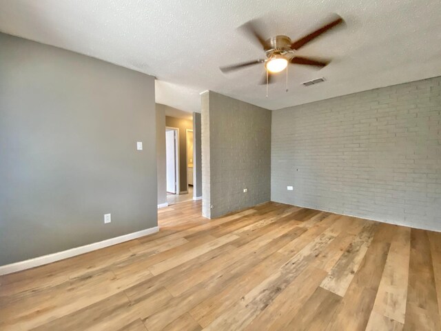 empty room featuring ceiling fan, a textured ceiling, brick wall, and light wood-type flooring