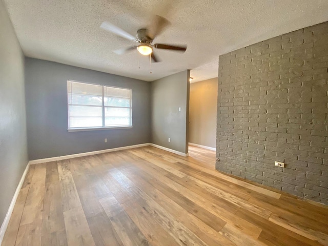 empty room with light hardwood / wood-style floors, ceiling fan, a textured ceiling, and brick wall