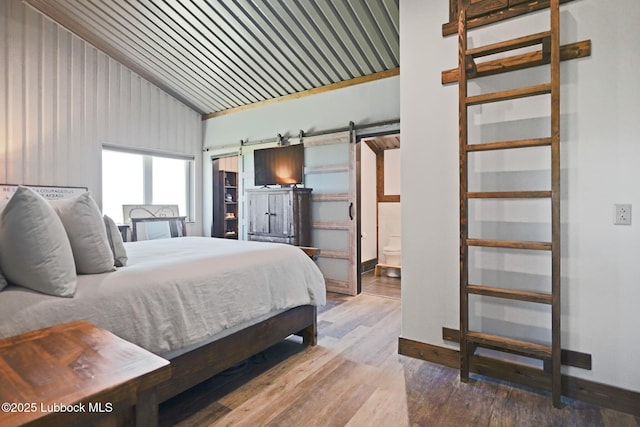 743 Co Rd, M, Tahoka, TX 79373 - bedroom featuring lofted ceiling, a barn door, wood finished floors, baseboards, and ensuite bathroom