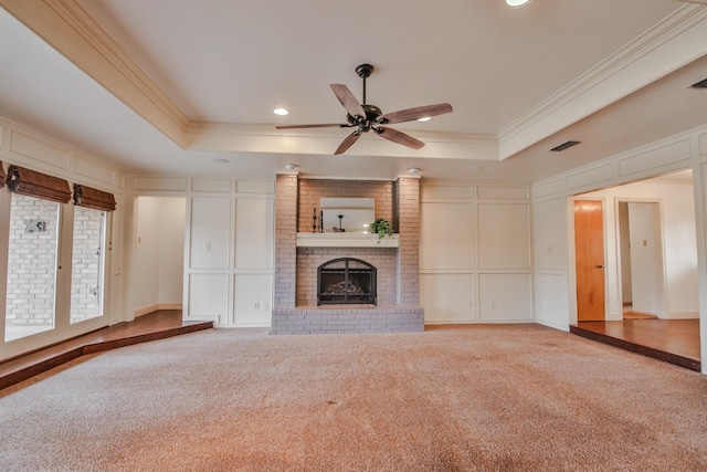 unfurnished living room featuring a brick fireplace, a tray ceiling, carpet floors, and ornamental molding