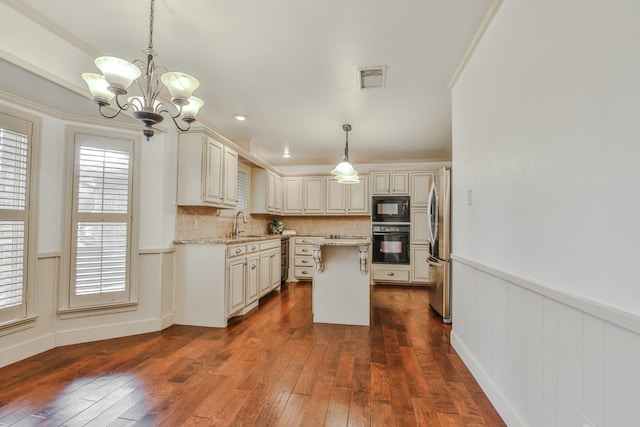 kitchen featuring dark hardwood / wood-style floors, backsplash, hanging light fixtures, light stone counters, and black appliances