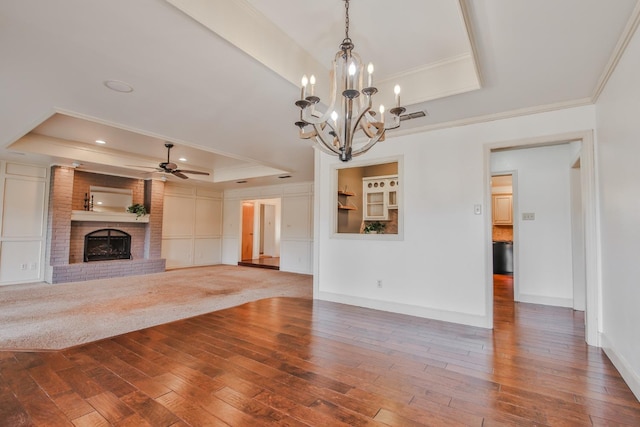 unfurnished living room featuring crown molding, hardwood / wood-style flooring, ceiling fan, a brick fireplace, and a raised ceiling