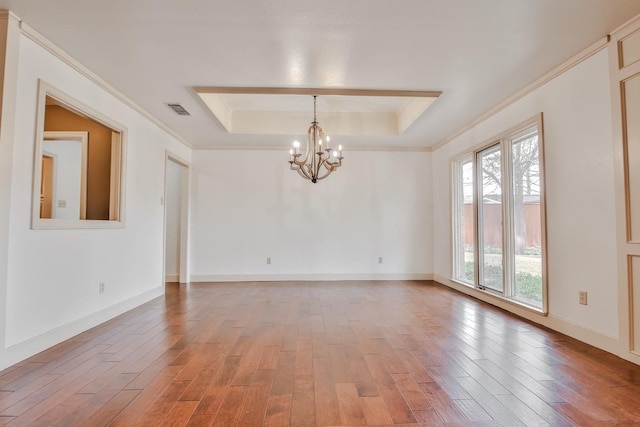 spare room with crown molding, hardwood / wood-style floors, a tray ceiling, and a chandelier