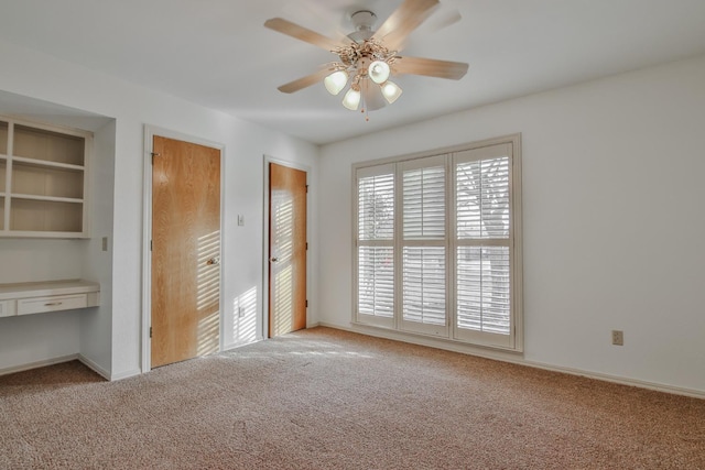 unfurnished bedroom with light carpet, ceiling fan, built in desk, and multiple closets