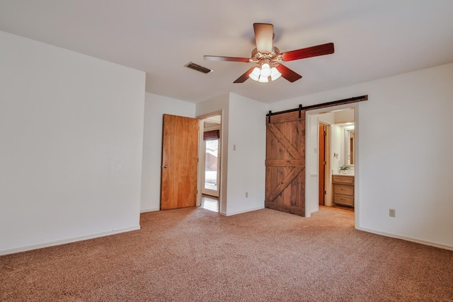 unfurnished bedroom featuring ceiling fan, ensuite bath, a barn door, and light carpet