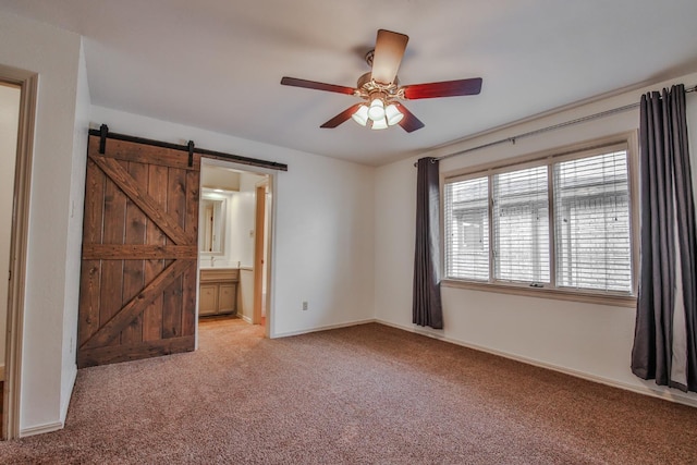 unfurnished bedroom featuring ceiling fan, ensuite bath, a barn door, and light carpet