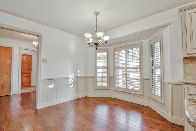 unfurnished dining area featuring hardwood / wood-style floors, crown molding, and a chandelier