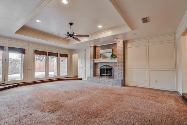 unfurnished living room featuring crown molding, a fireplace, a raised ceiling, and light carpet