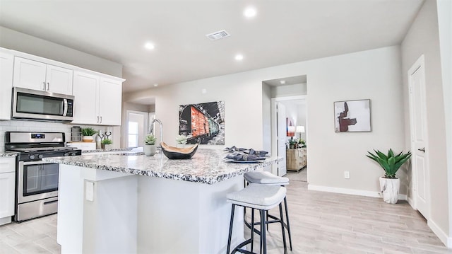 kitchen with appliances with stainless steel finishes, a breakfast bar, a center island with sink, and white cabinets