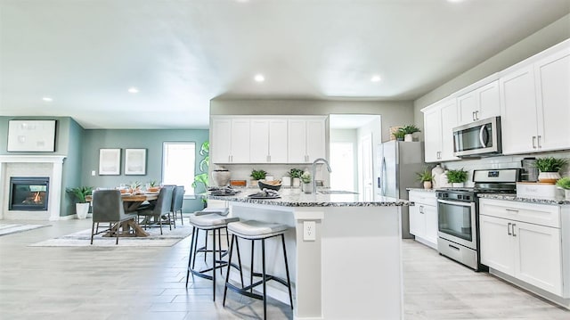 kitchen with white cabinetry, stainless steel appliances, light stone countertops, and a kitchen island with sink