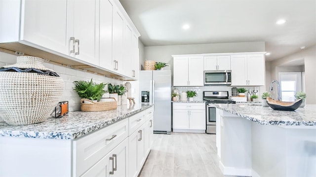 kitchen with light stone counters, stainless steel appliances, light hardwood / wood-style floors, and white cabinets