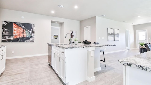 kitchen with sink, white cabinetry, stainless steel dishwasher, an island with sink, and light stone countertops