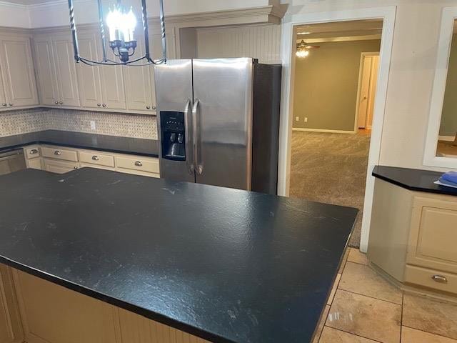 kitchen with decorative backsplash, dark stone counters, light tile patterned floors, stainless steel refrigerator with ice dispenser, and an inviting chandelier