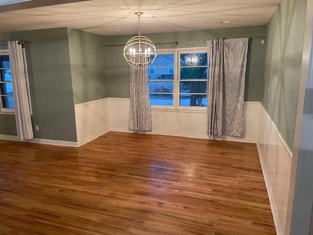 unfurnished dining area with wood-type flooring and a notable chandelier