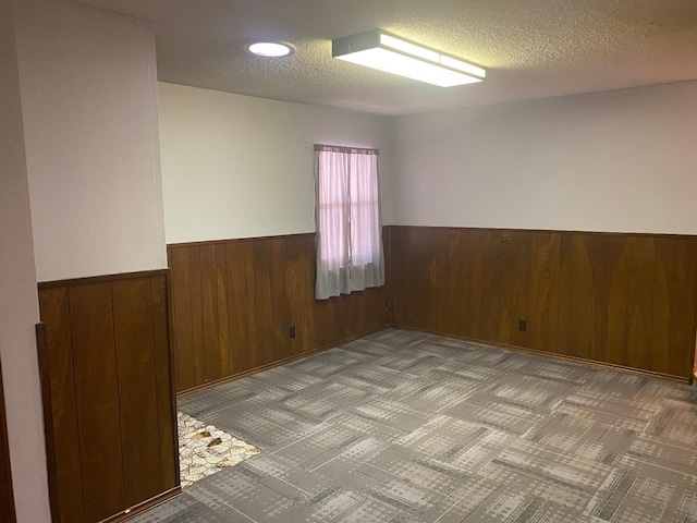 unfurnished room featuring light carpet, a textured ceiling, and wood walls