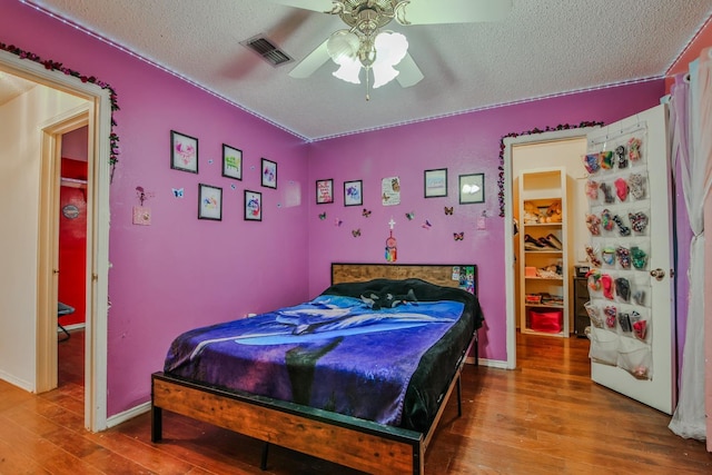 bedroom with ceiling fan, wood-type flooring, and a textured ceiling