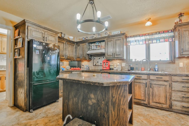 kitchen with sink, black refrigerator, dark stone countertops, a center island, and tasteful backsplash