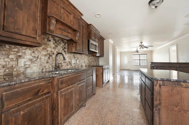 kitchen with sink, dark stone countertops, tasteful backsplash, dark brown cabinetry, and a kitchen island