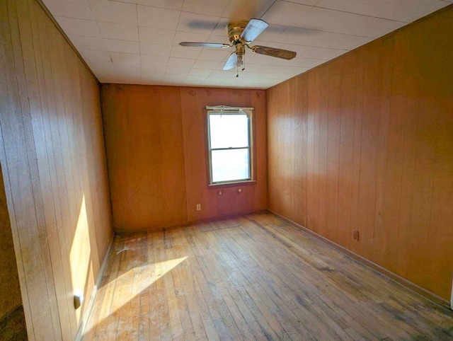 empty room with ceiling fan, light hardwood / wood-style floors, and wood walls