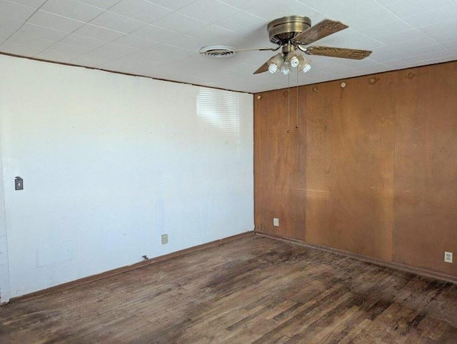 empty room with dark hardwood / wood-style flooring, ceiling fan, and wood walls