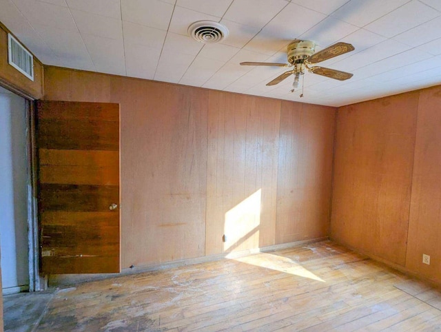 empty room with ceiling fan, light hardwood / wood-style flooring, and wood walls