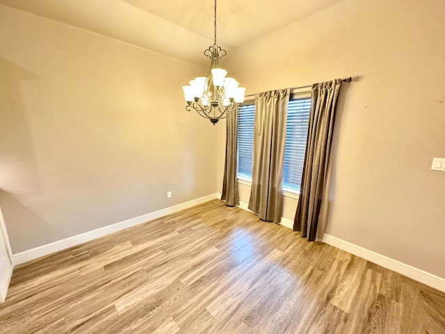 spare room featuring an inviting chandelier, lofted ceiling, and hardwood / wood-style floors