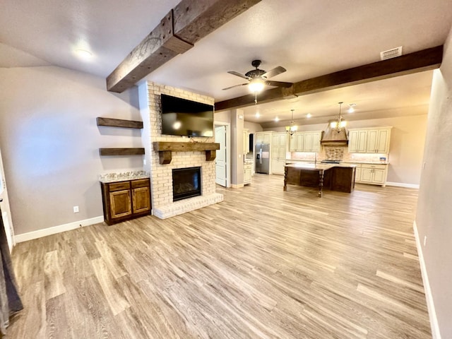 unfurnished living room featuring a brick fireplace, ceiling fan with notable chandelier, beam ceiling, and light hardwood / wood-style floors