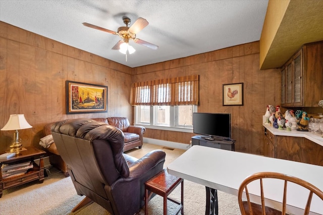 carpeted living area featuring a ceiling fan, visible vents, wood walls, and a textured ceiling