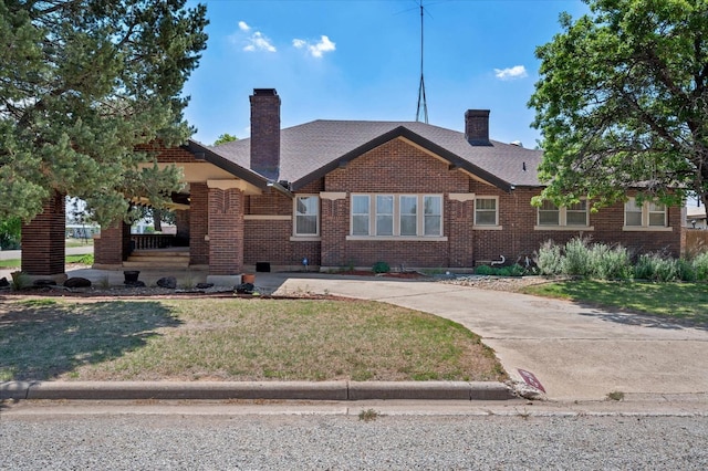 view of front of home with brick siding, covered porch, a chimney, and a front lawn