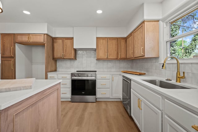 kitchen with stainless steel appliances, light countertops, a sink, light wood-style floors, and tasteful backsplash