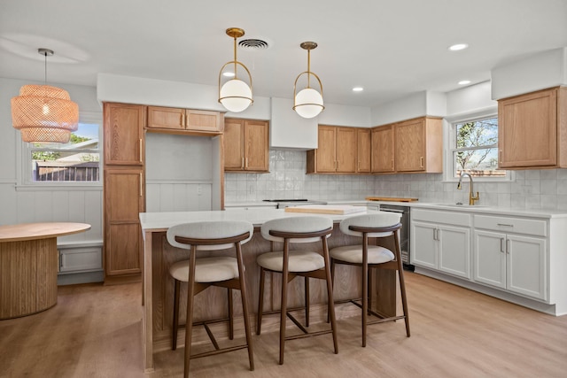 kitchen featuring a center island, tasteful backsplash, a sink, light wood-style flooring, and light countertops