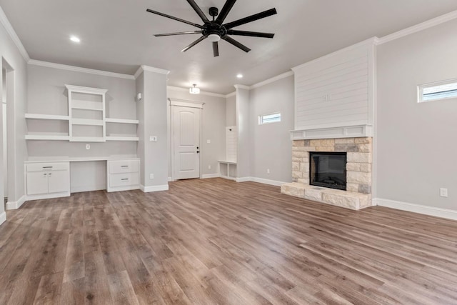 unfurnished living room featuring ornamental molding, a stone fireplace, built in desk, and light hardwood / wood-style floors