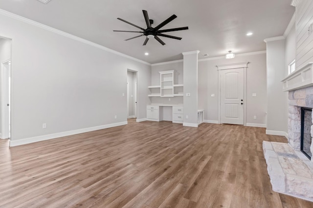 unfurnished living room featuring a stone fireplace, built in desk, ornamental molding, ceiling fan, and light hardwood / wood-style flooring